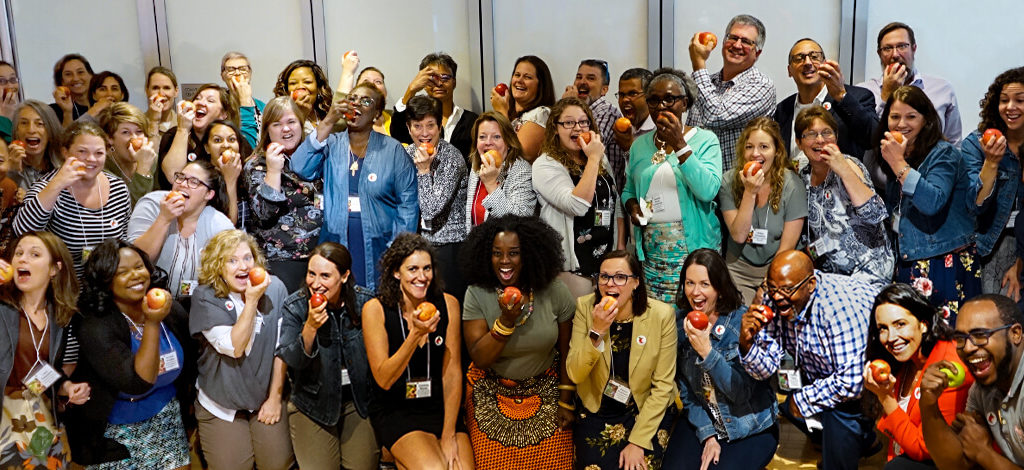 Group Of People Smiling, Biting Into Apples